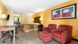 A hotel room with a bed, desk, chair, and ottoman. - Rodeway Inn (Greenwood)