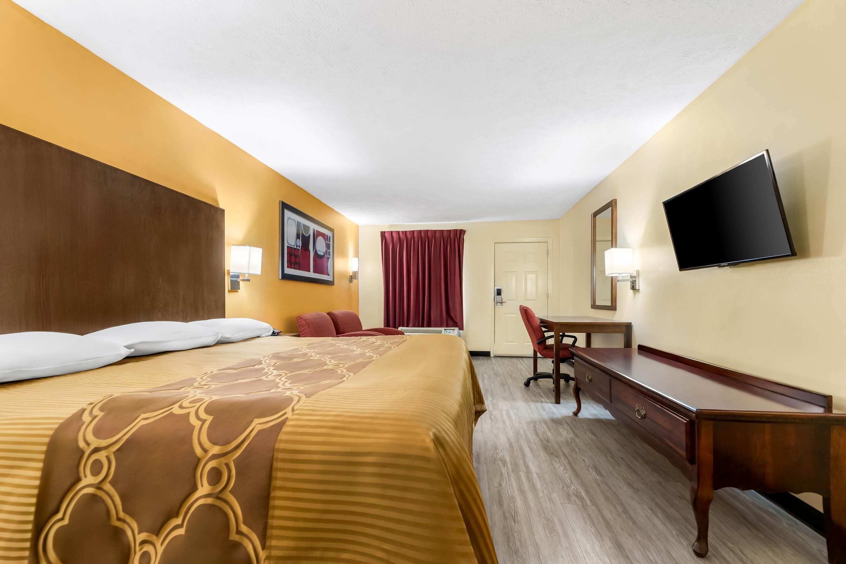 A hotel room with a bed, a desk, a chair, a television, and a door.