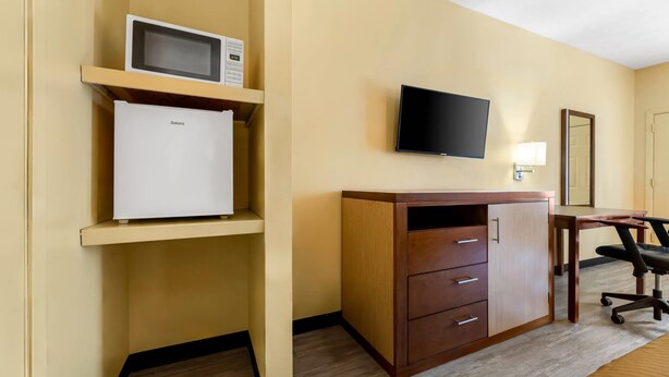 A hotel room with a wooden desk, a flat-screen TV, a microwave, and a refrigerator. - Rodeway Inn (Greenwood)