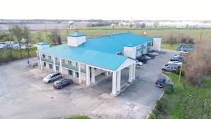 A two-story building with a blue roof, a parking lot with several cars, and a grassy area with trees.