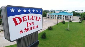 A sign for the Deluxe Inn & Suites with a building in the background. - Rodeway Inn (Greenwood)