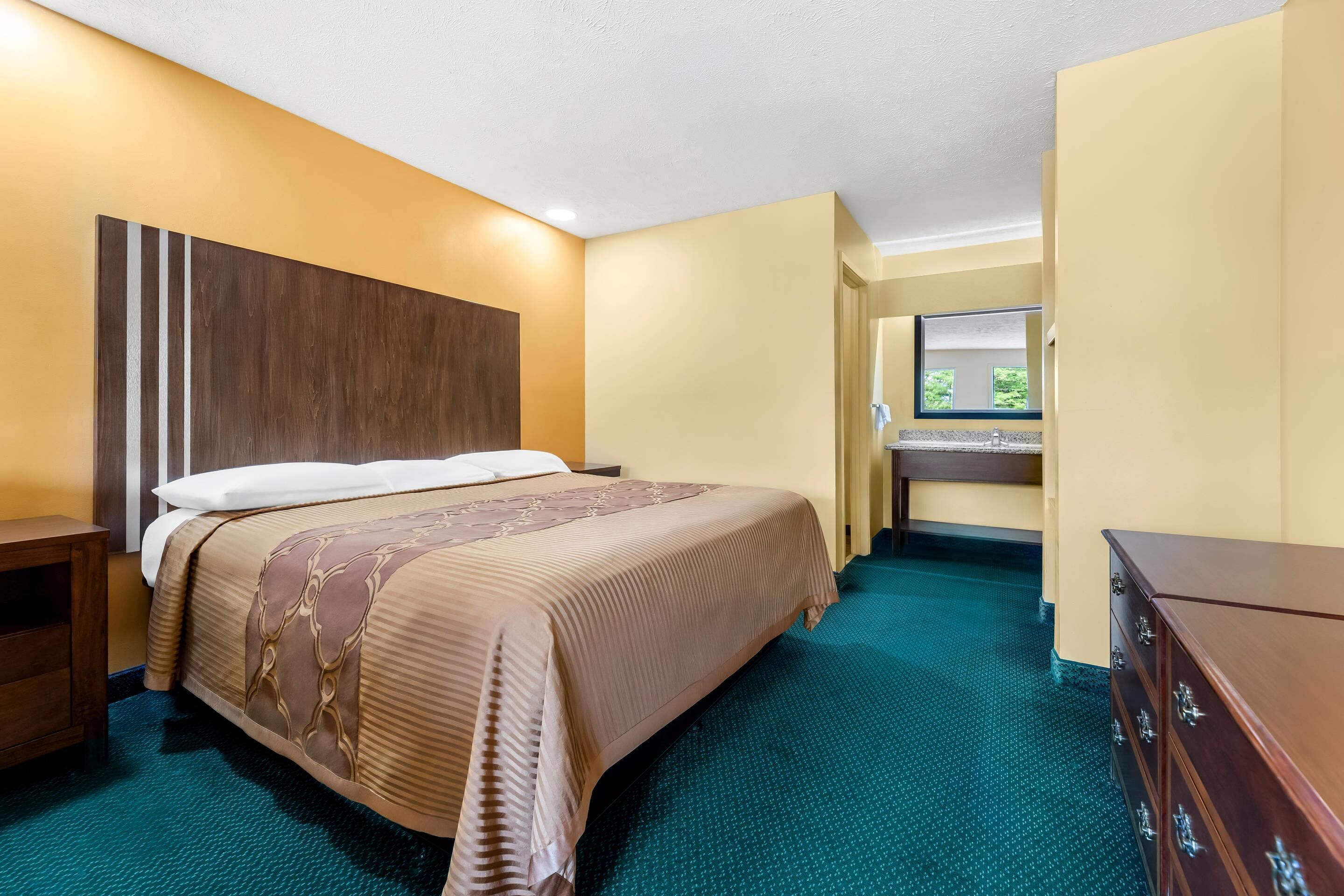 A hotel room with a bed, a dresser, a desk with a mirror, and a view of the outdoors.