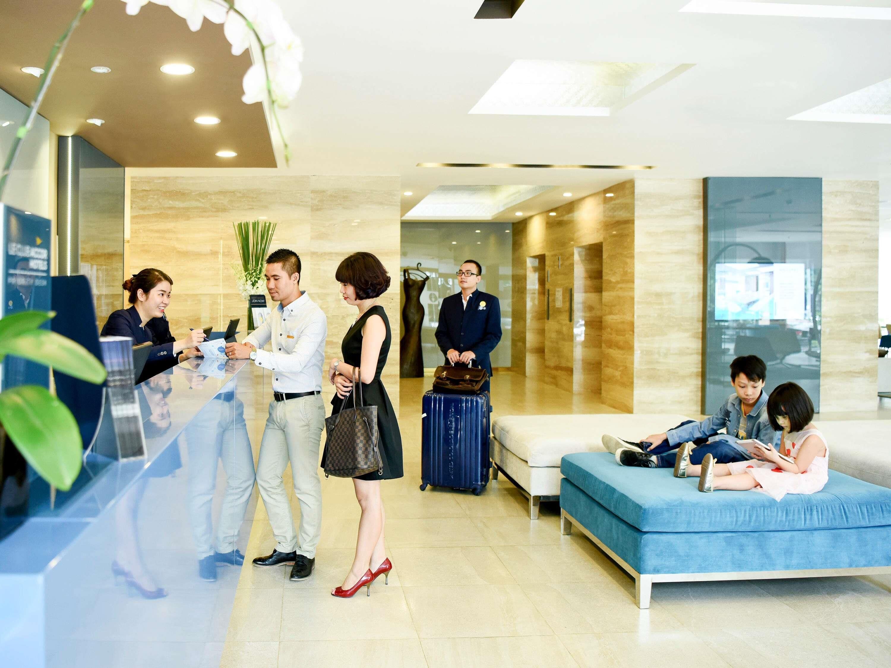 A hotel reception area with a reception desk, a seating area with a sofa, and a wall-mounted TV.