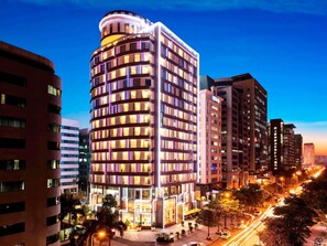 Un hĂŽtel Ă plusieurs Ă©tages, dotĂ© dâune façade incurvĂ©e, de fenĂȘtres illuminĂ©es et dâune entrĂ©e centrale.