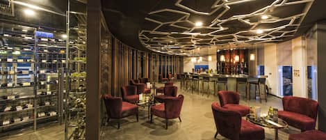 A modern bar area with red upholstered chairs, a bar counter, and a wine rack visible through a glass partition.