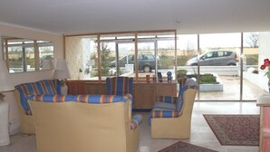 Una sala de estar con sofá, sillones, una mesa de centro y un ventanal que ofrece vistas a coches estacionados afuera.