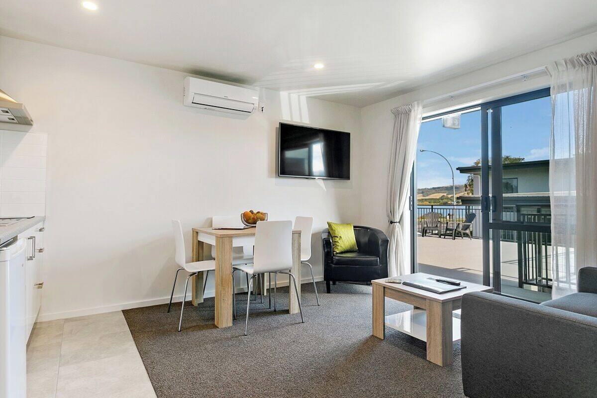 A modern living room with a flat-screen TV, a dining area with a table and chairs, a sofa, and a balcony with a view.