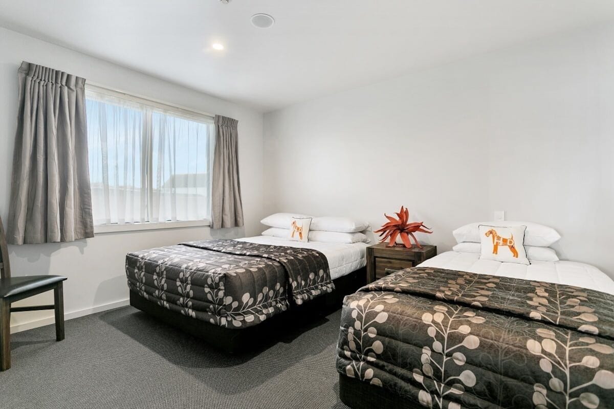 A hotel room with two beds, a chair, and a window with curtains.