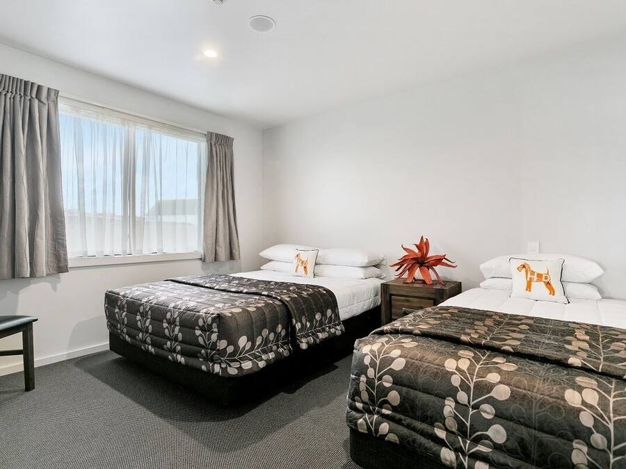 A hotel room with two beds, a chair, and a window with curtains.