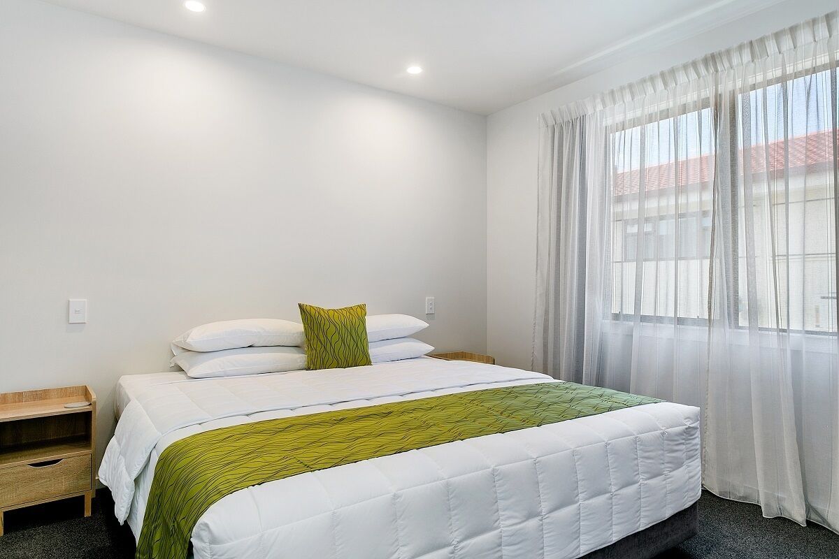A neatly arranged hotel room with a bed, a bedside table, and a window with sheer curtains.