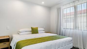 A neatly arranged hotel room with a bed, a bedside table, and a window with sheer curtains.