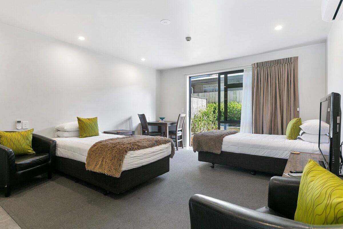 A modern hotel room with two beds, a sofa, a desk, and a TV.