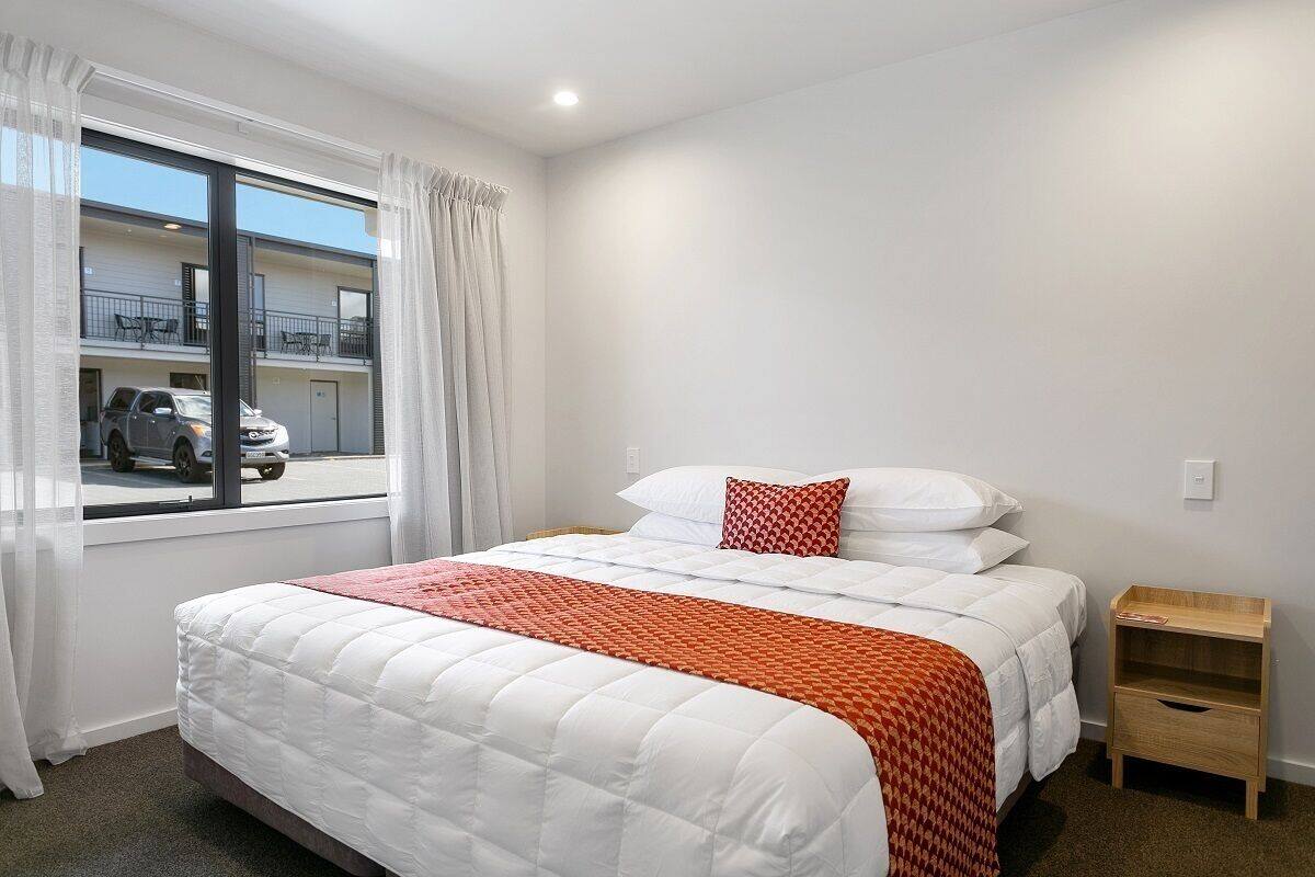 A hotel room with a large bed, a window with curtains, a wooden nightstand, and a view of the outside.