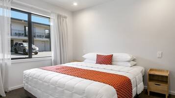 Habitación de hotel con una cama grande, una ventana con cortinas, una mesita de noche de madera y vistas al exterior.