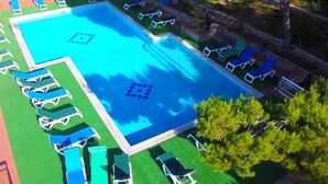Une grande piscine rectangulaire dont le centre est bleu, entourée de chaises longues blanches et d’une pelouse verte.