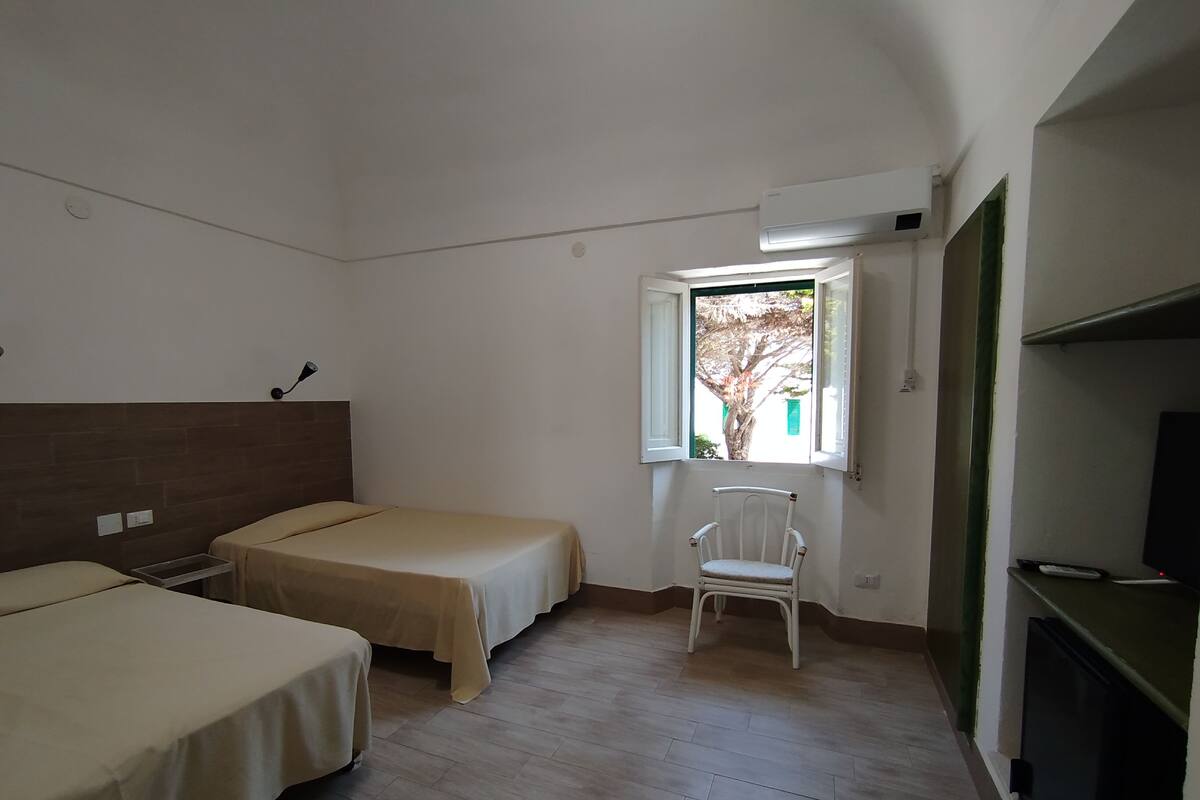 A room with two beds, a chair, a window, and a TV.