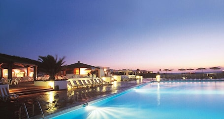 A swimming pool with lounge chairs and umbrellas, surrounded by buildings with outdoor seating areas.