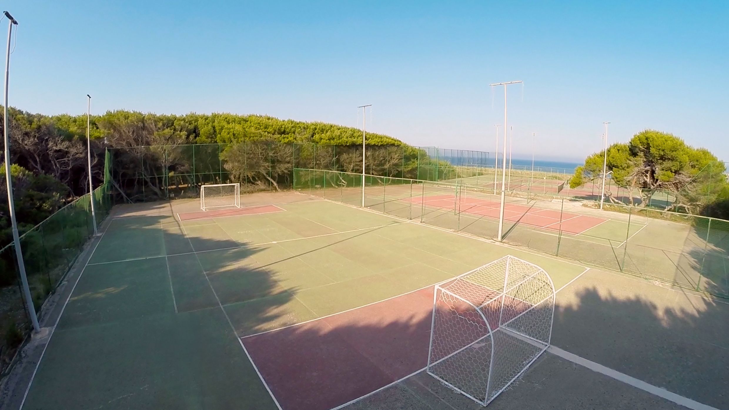 Un campo da tennis all'aperto con una rete, circondato da una recinzione e alberi.