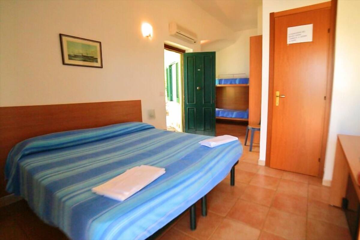 A hotel room with a bed, a desk with a television, and a green door.
