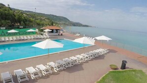A pool area with lounge chairs and umbrellas, a small building, and a view of the sea. - Sabbie Bianche (Parghelia)