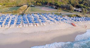 A beach with rows of white lounge chairs and blue umbrellas.