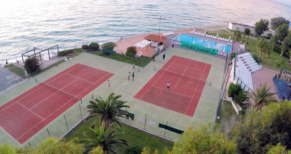 A tennis court with a pool adjacent to a beach.