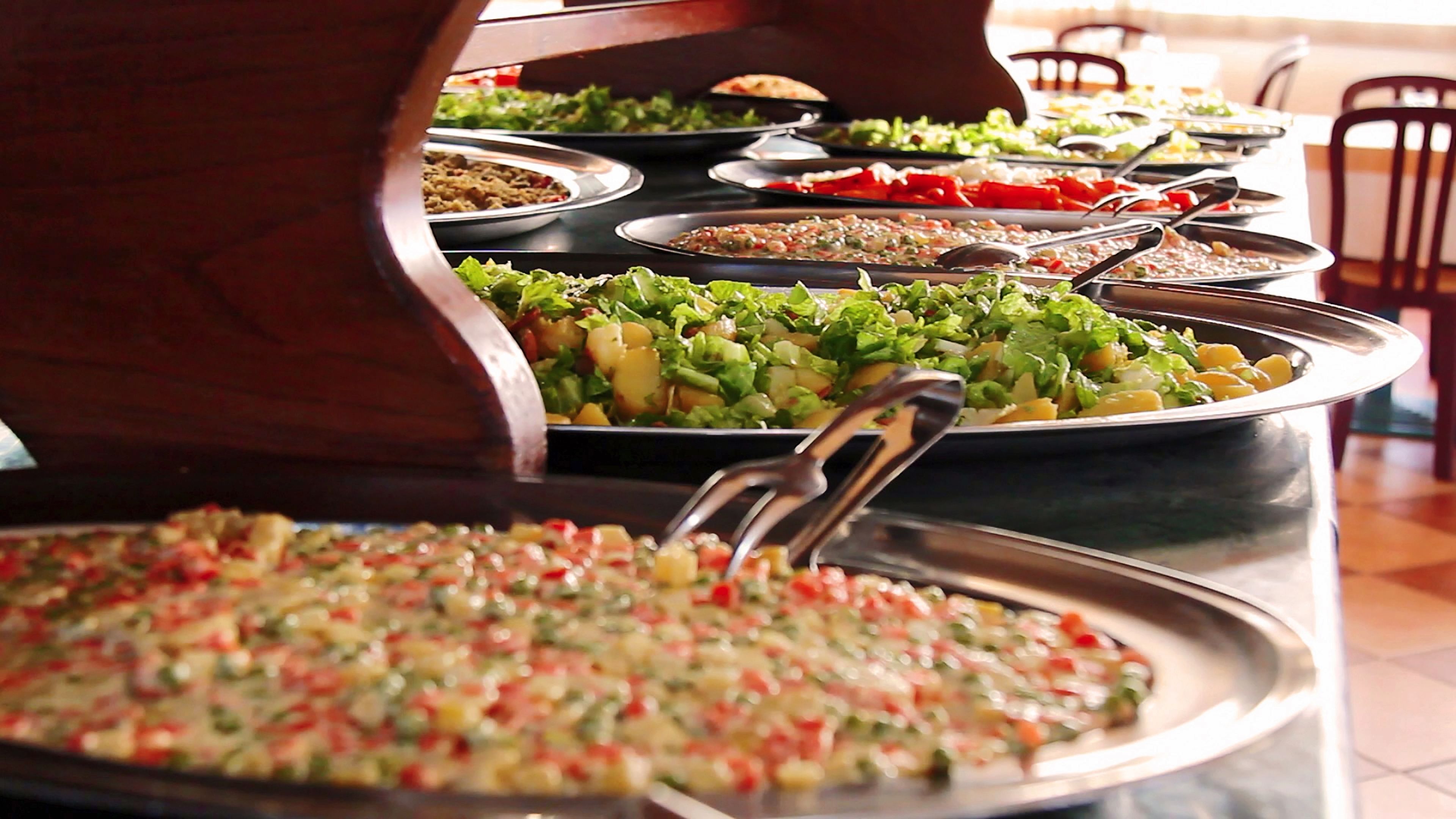 Un buffet con diversi piatti, tra cui insalate e un piatto di pasta, serviti su vassoi metallici.