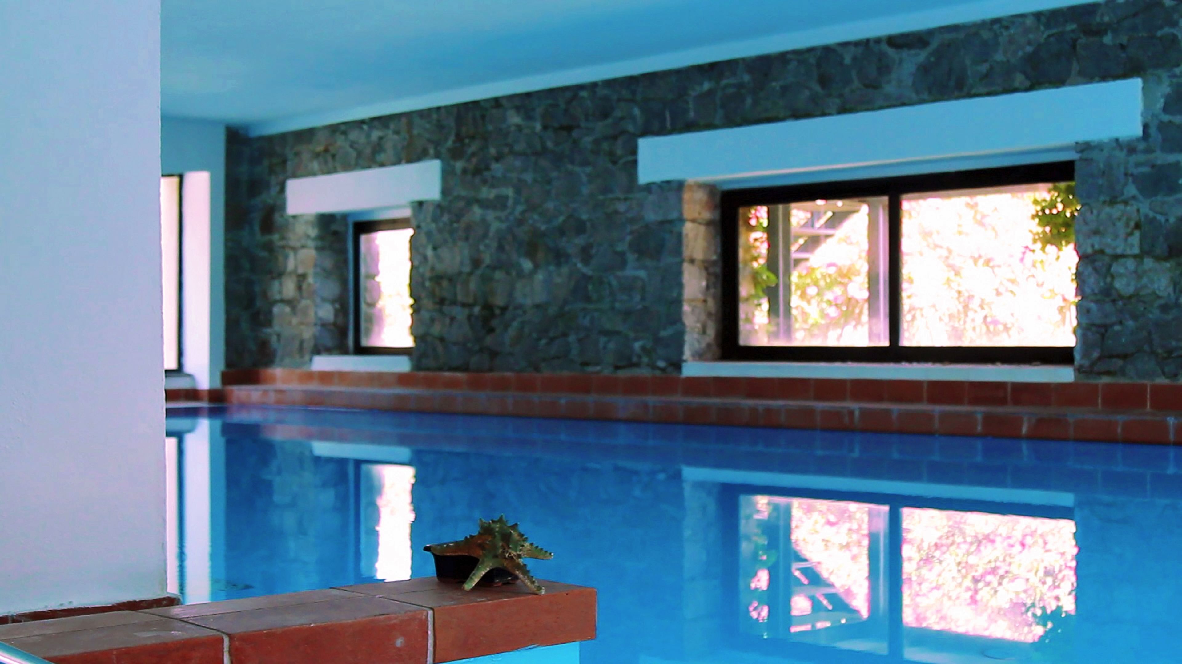 Piscina con pareti in pietra e finestre che riflettono l'esterno.