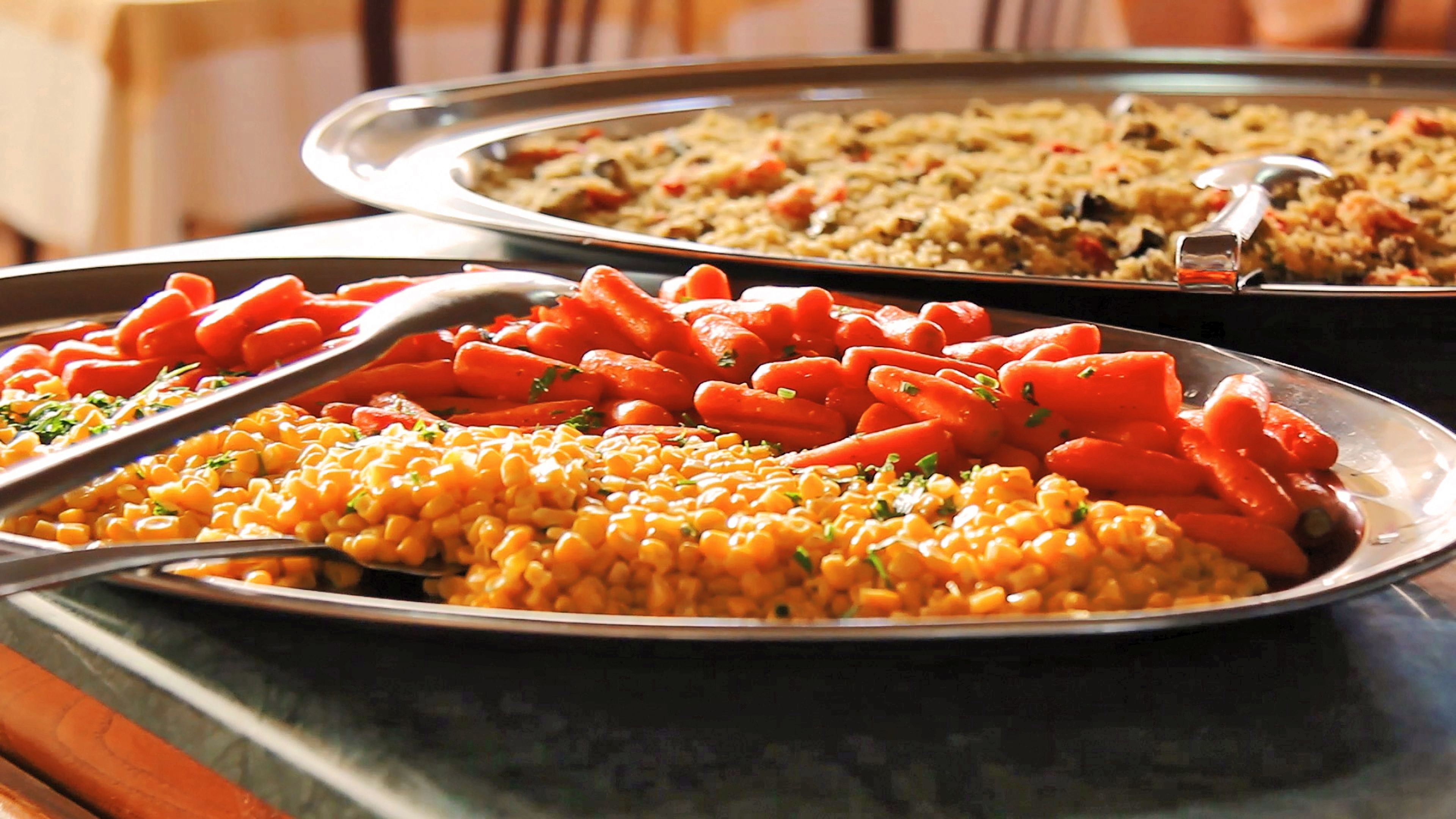 A buffet table with various dishes including macaroni, carrots, and a rice dish.