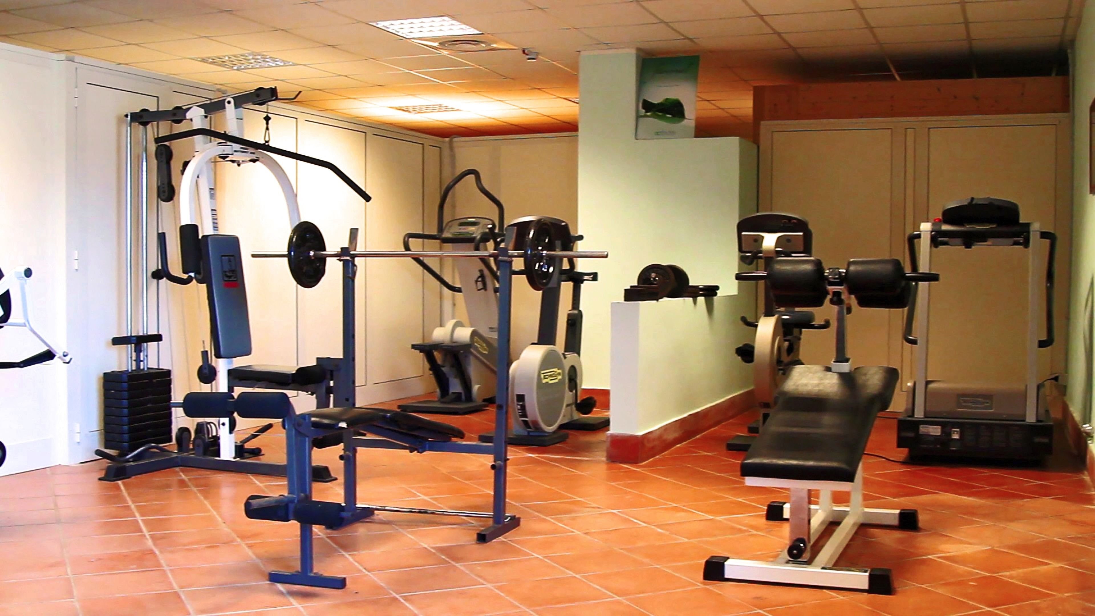 Une salle de sport équipée de divers appareils d’exercice, notamment un banc de développé couché, des appareils de musculation et un tapis de course.