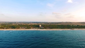 A coastal landscape with a beach, a building with a pool, and a hilly background. - Villaggio dei Pini (Sorso)