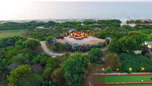 An outdoor amphitheater surrounded by lush greenery and a beach in the background. - Villaggio dei Pini (Sorso)