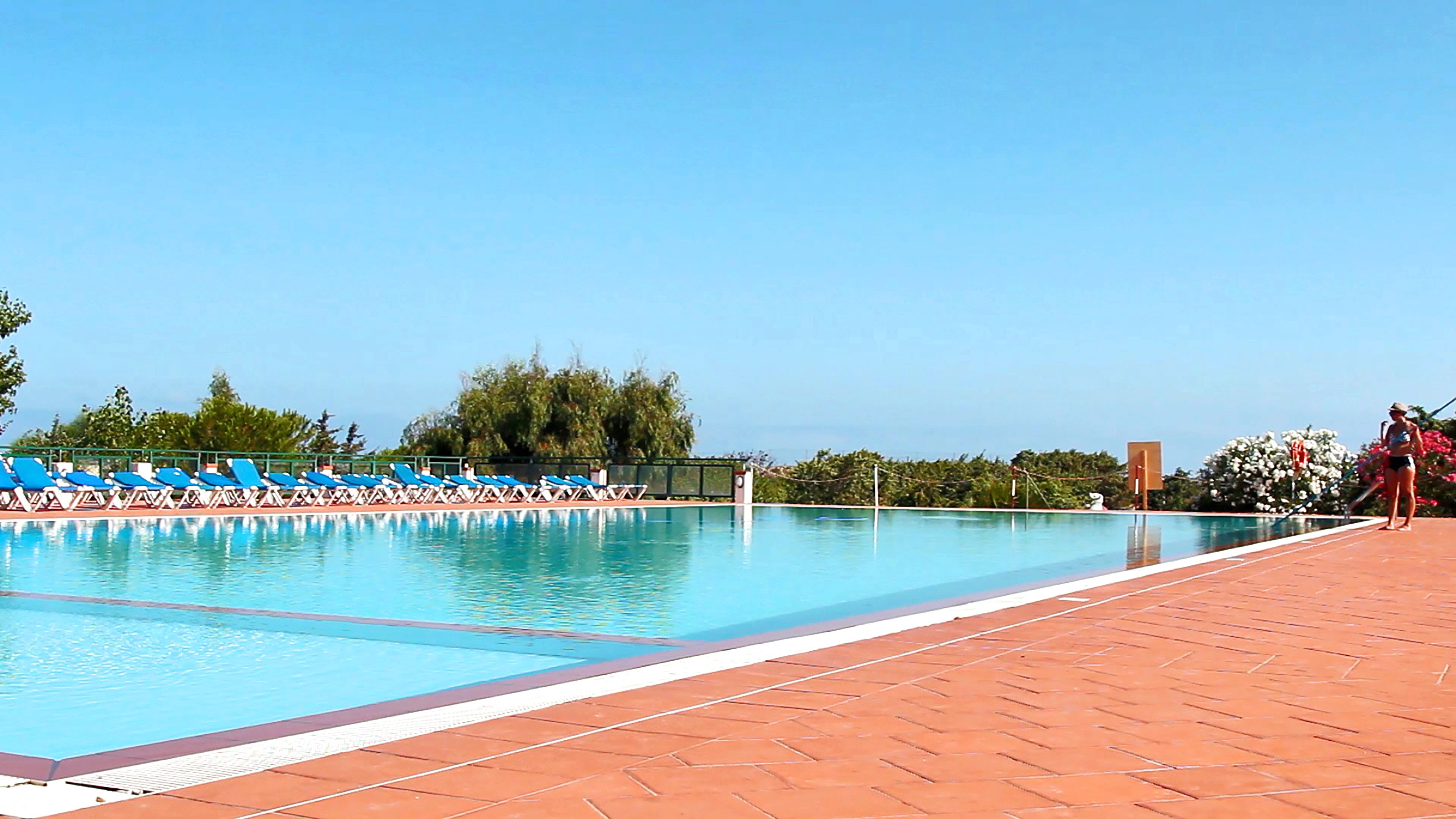Una piscina con lettini blu e un solarium piastrellato.