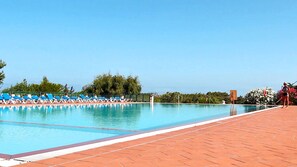 A swimming pool with blue lounge chairs and a tiled deck. - Villaggio dei Pini (Sorso)