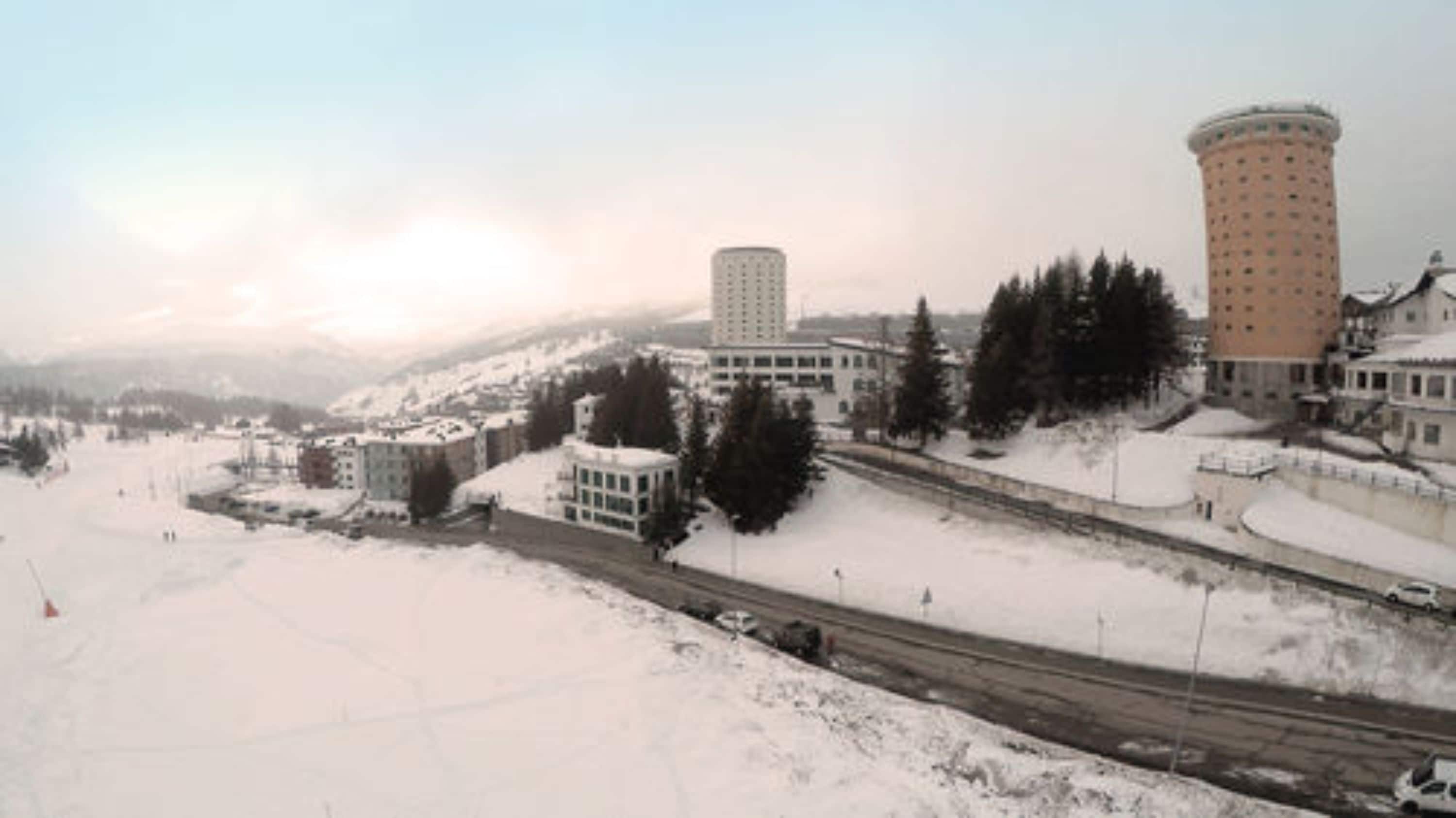 A snowy landscape with buildings, including a tall cylindrical structure and a rectangular building with multiple windows.