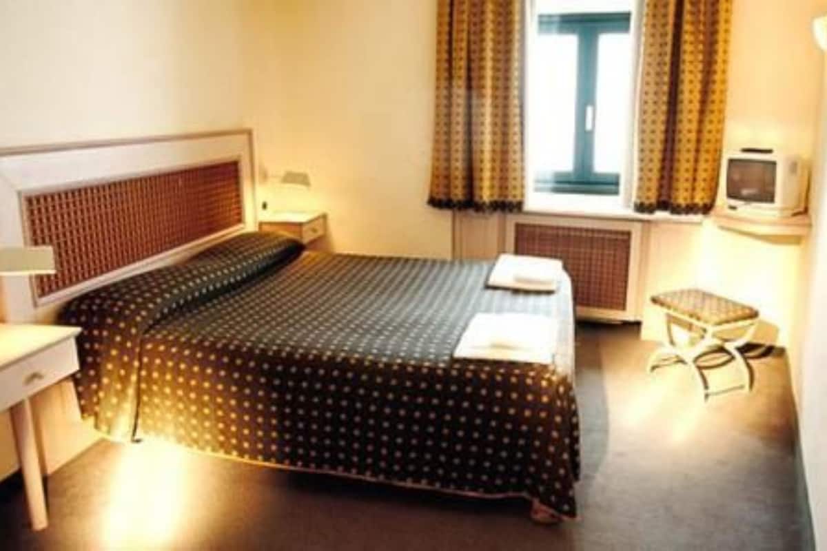 Una habitación de hotel con una cama, una mesita, una silla, un televisor y una ventana con cortinas.
