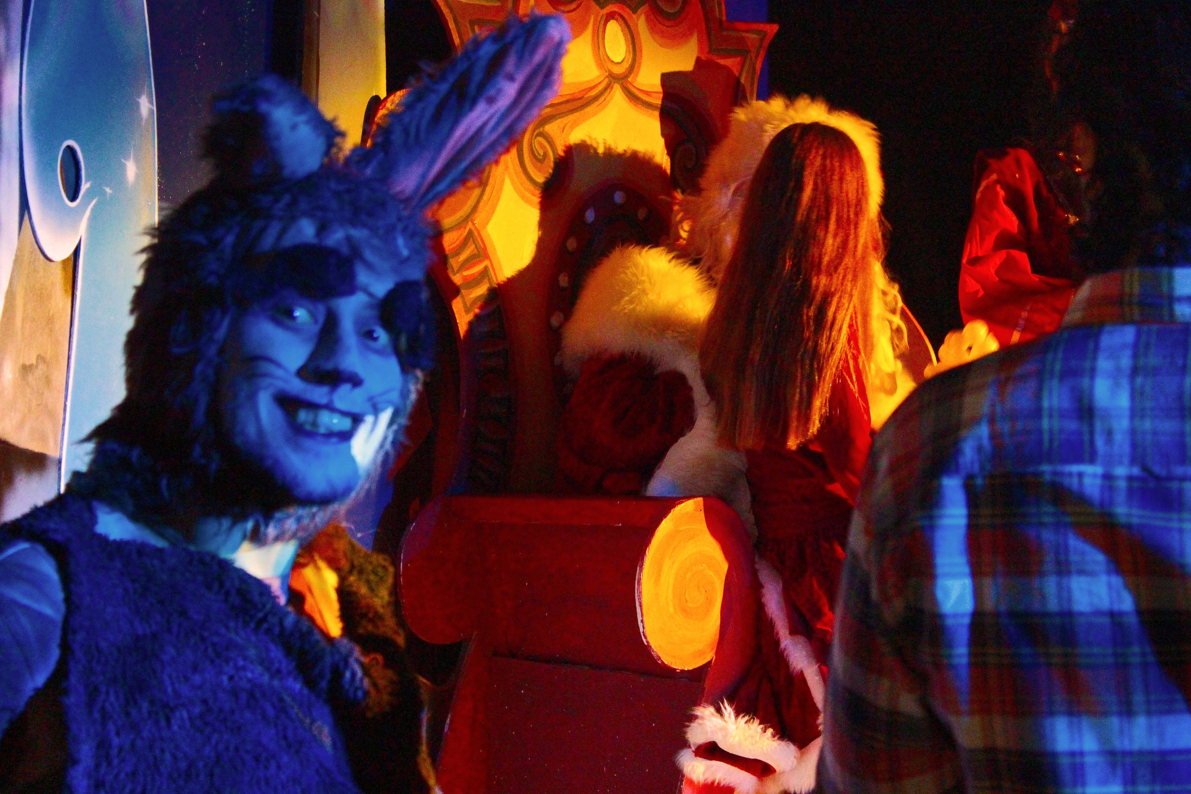A group of people in festive costumes, including a character resembling Santa Claus, in a dimly lit indoor setting.