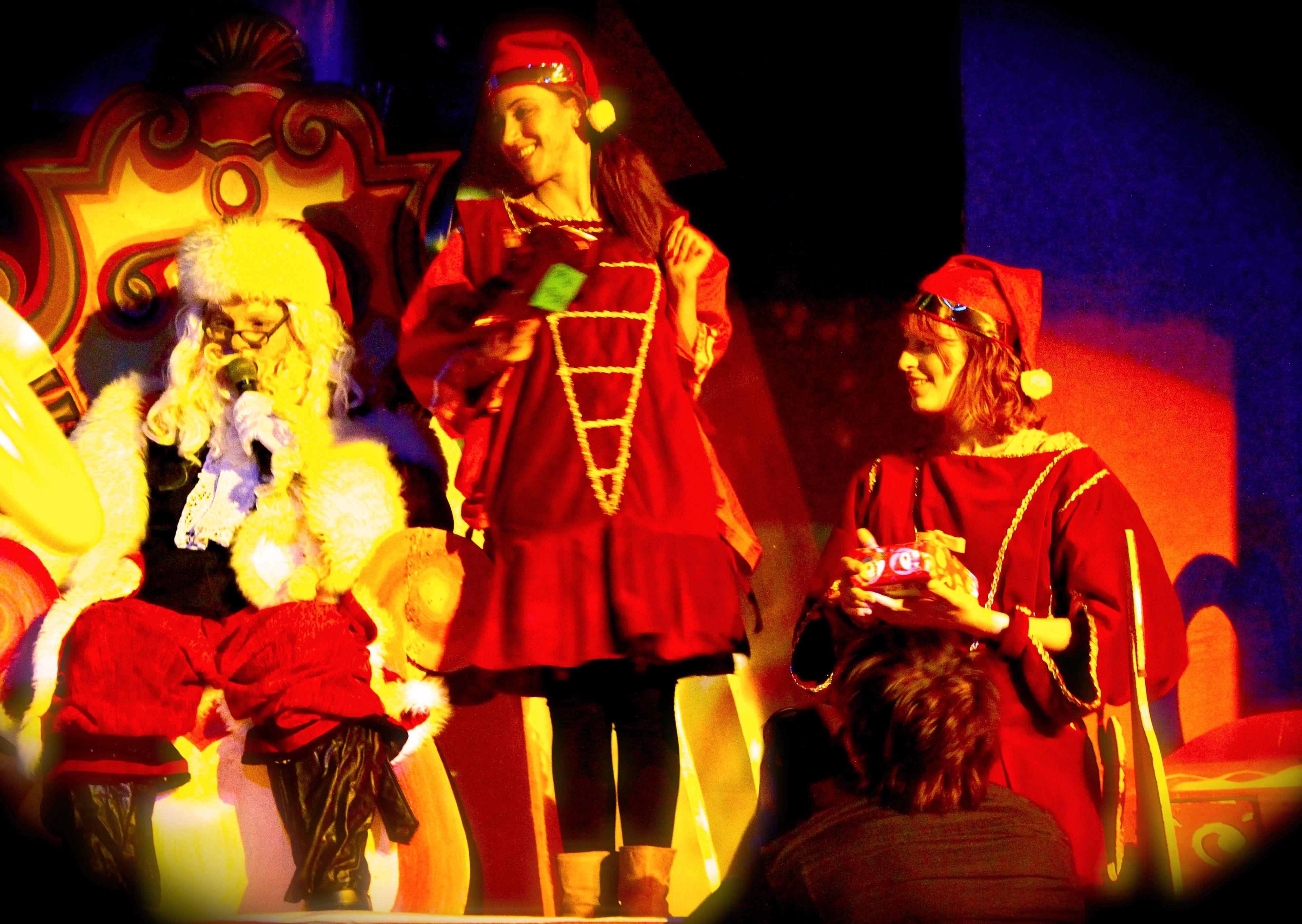 Un palcoscenico con artisti in costumi rossi, un'enorme scenografia simile a un albero di Natale e un membro del pubblico seduto.