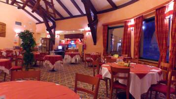 Ein Restaurant mit mehreren Tischen und Stühlen, Holzbalken an der Decke und einem großen Fenster mit Vorhängen.