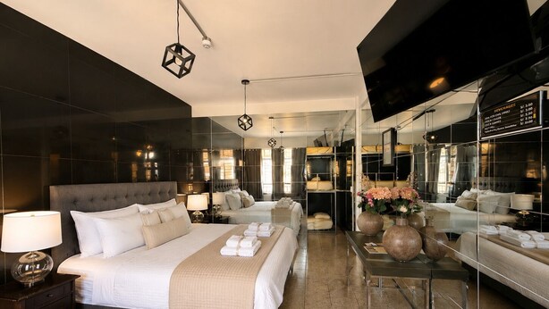 A modern hotel room with a large bed, bedside tables, a mirror, and a glass partition. - Ica Adventures II - Hostel (Ica)