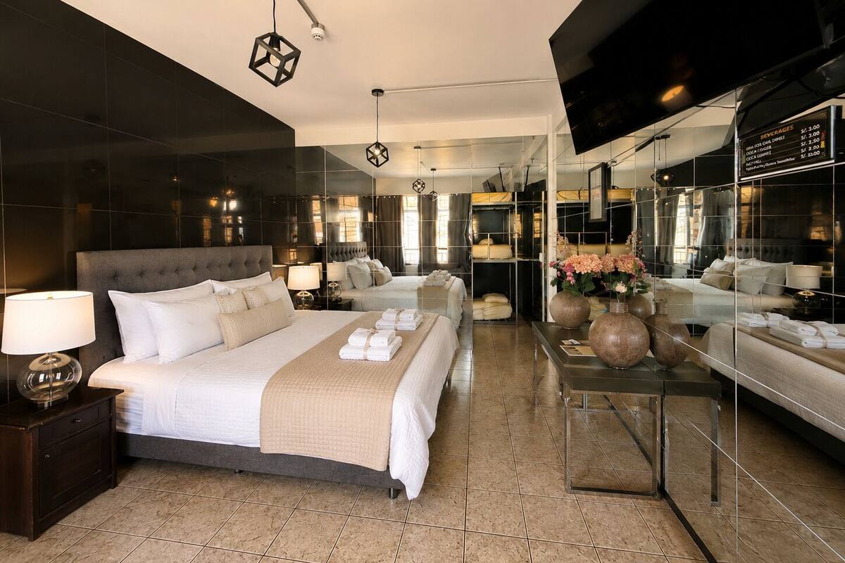 A modern hotel room with a large bed, bedside tables, a mirror, and a glass partition.