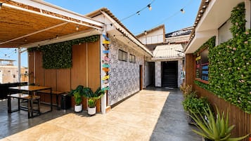 Um pátio com pérgola de madeira, plantas em vasos, uma parede com placas de sinalização e um edifício com a placa 'Hostel La Aventura'.
