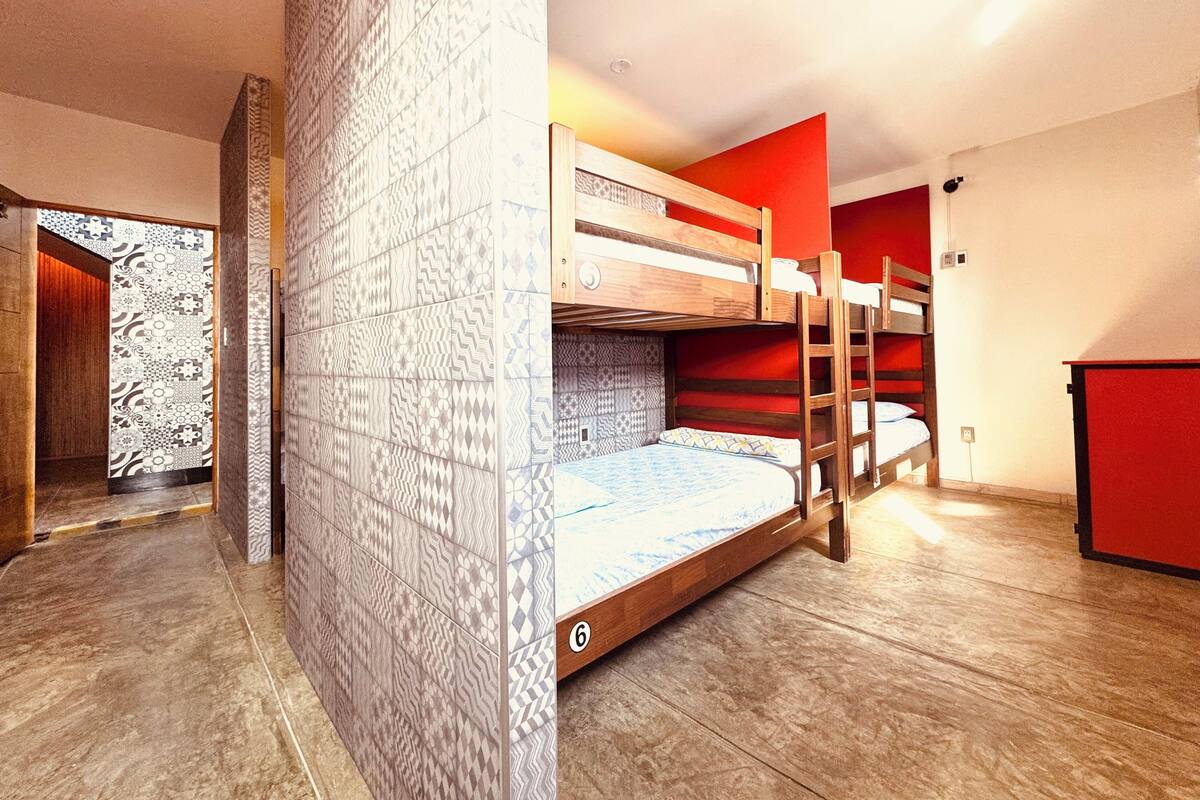 A bunk bed room with patterned walls, a wooden floor, and a red accent wall.