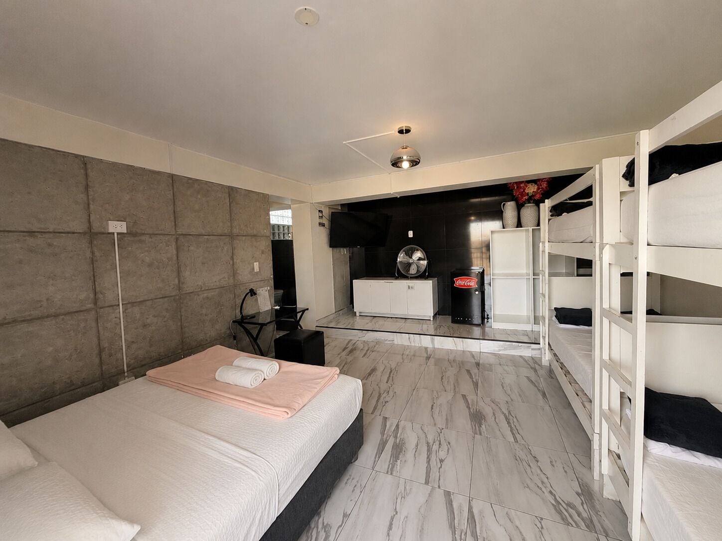 Quarto de hotel moderno com cama, escrivaninha, área de estar e cozinha compacta.