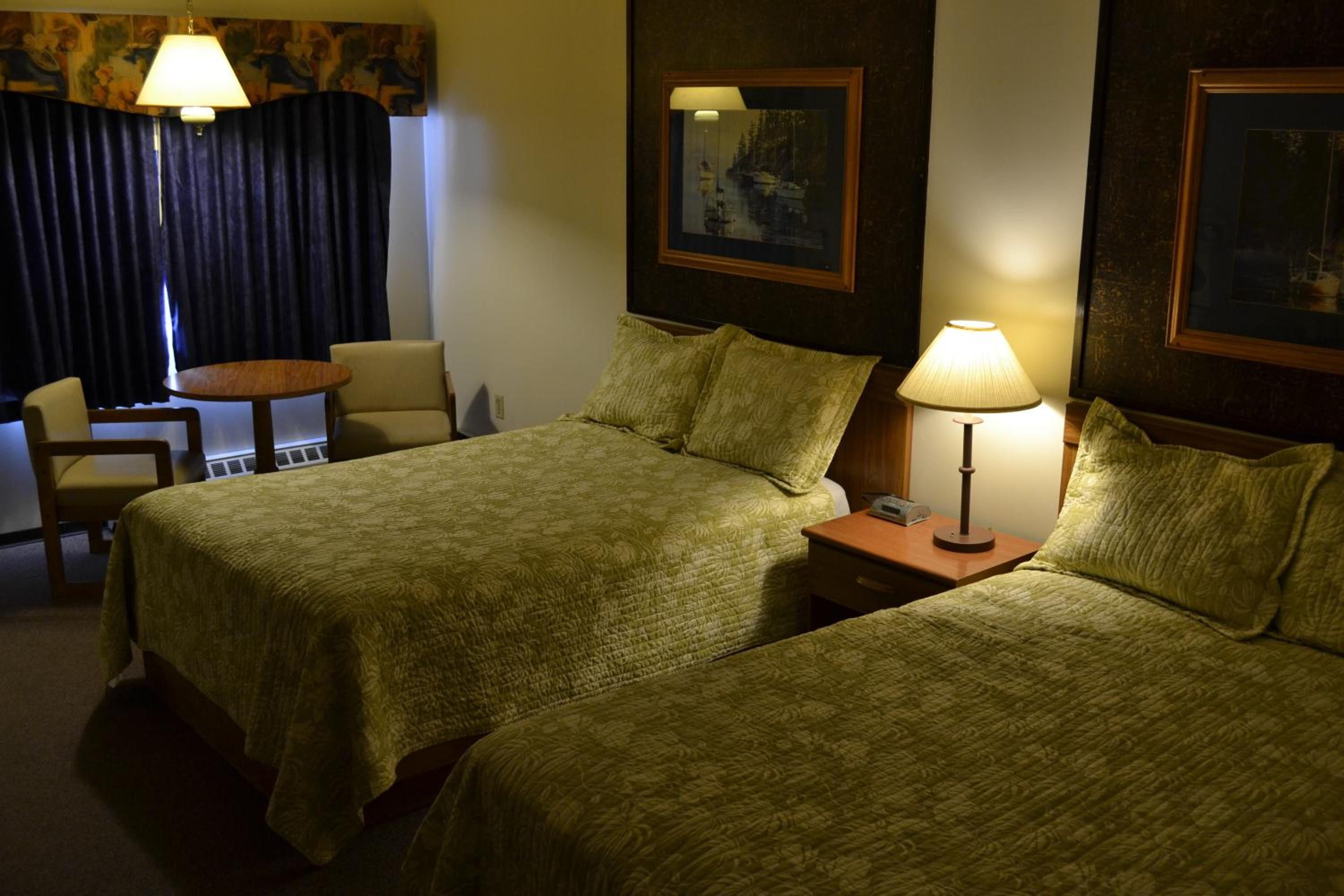 A hotel room with two beds, a desk, a chair, and a lamp.