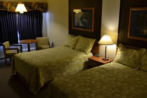 A hotel room with two beds, a desk, a chair, and a lamp. - Ranchmen Motel (Medicine Hat)