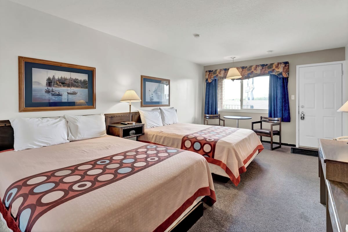A hotel room with two beds, a desk, a chair, and a window with curtains.