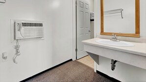 A hotel bathroom with a white sink, a mirror, and a wall-mounted heater. - Ranchmen Motel (Medicine Hat)