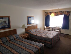 A hotel room with two beds, a desk, a chair, and a small table. - Ranchmen Motel (Medicine Hat)