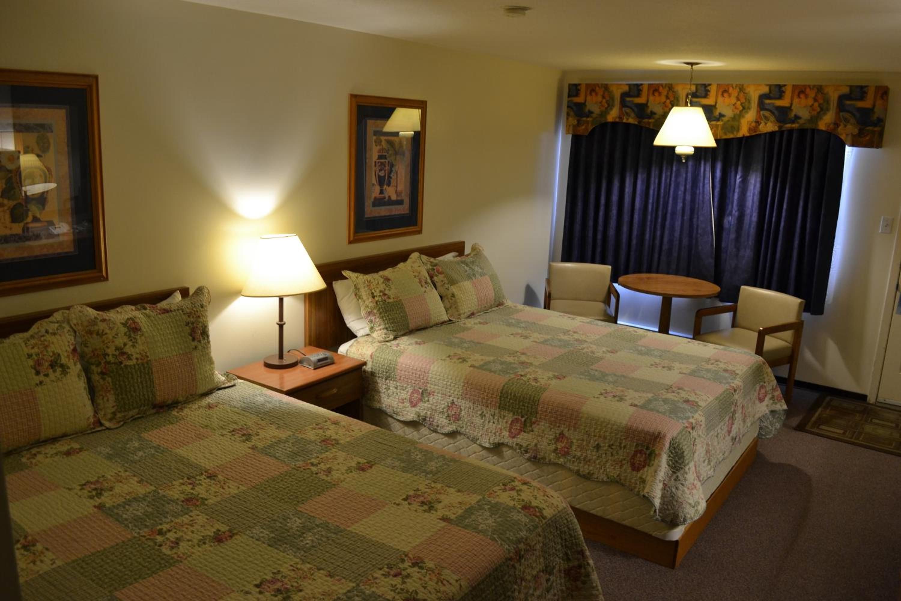 A hotel room with two beds, a desk, a chair, and a small table.